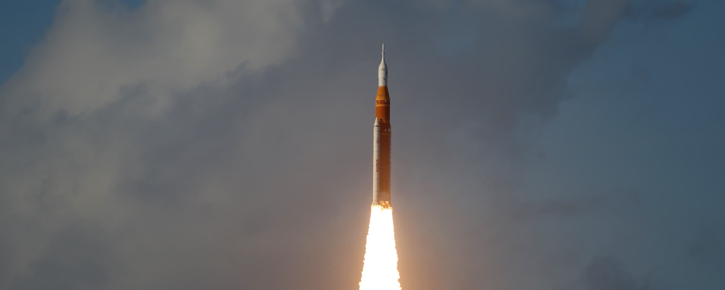 Artemis II lifts off atop the SLS rocket, climbing skyward on a column of flame.